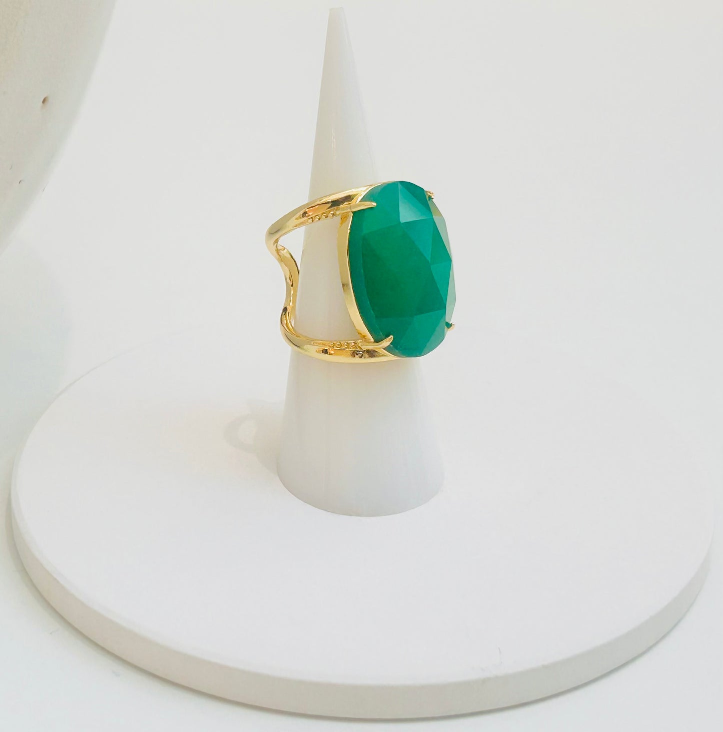 
                  
                    A gold ring with a large, faceted green jade gemstone, displayed on a white cone-shaped ring stand against a white background.
                  
                