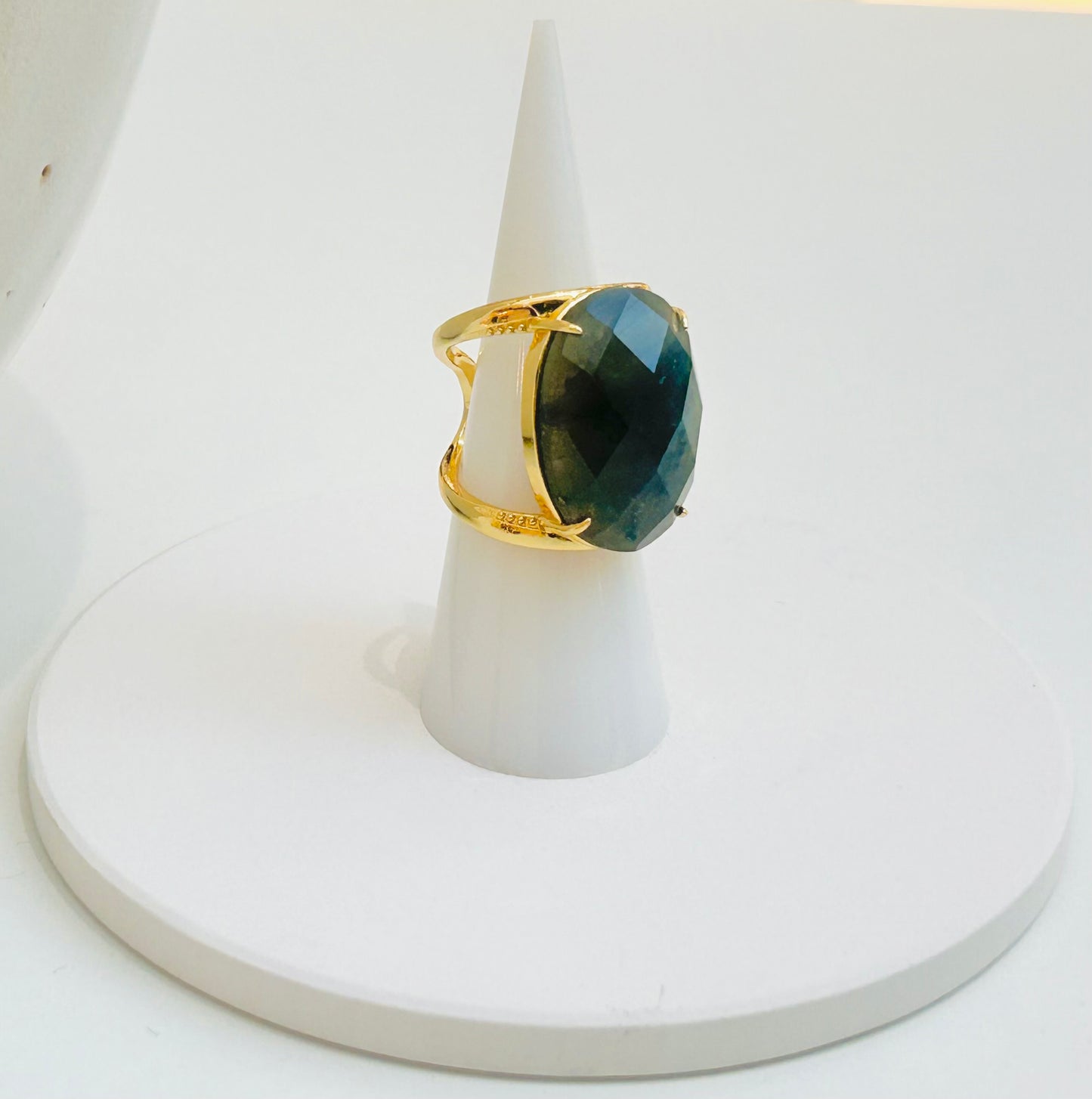
                  
                    A gold ring with a large oval labradorite faceted gemstone, displayed on a white cone stand against a white background.
                  
                