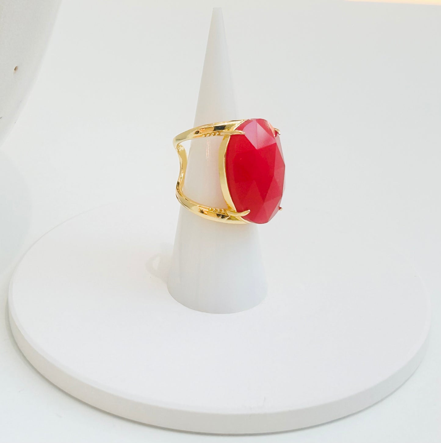 
                  
                    A gold ring with a large, faceted red jade gemstone, displayed on a white cone stand against a white background.
                  
                