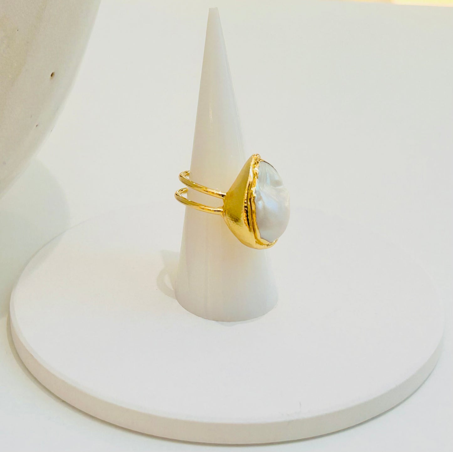 
                  
                    Avenelle Freshwater Pearl Statement Ring displayed on a white jewellery stand, featuring a natural oval pearl in a textured gold-plated setting.
                  
                