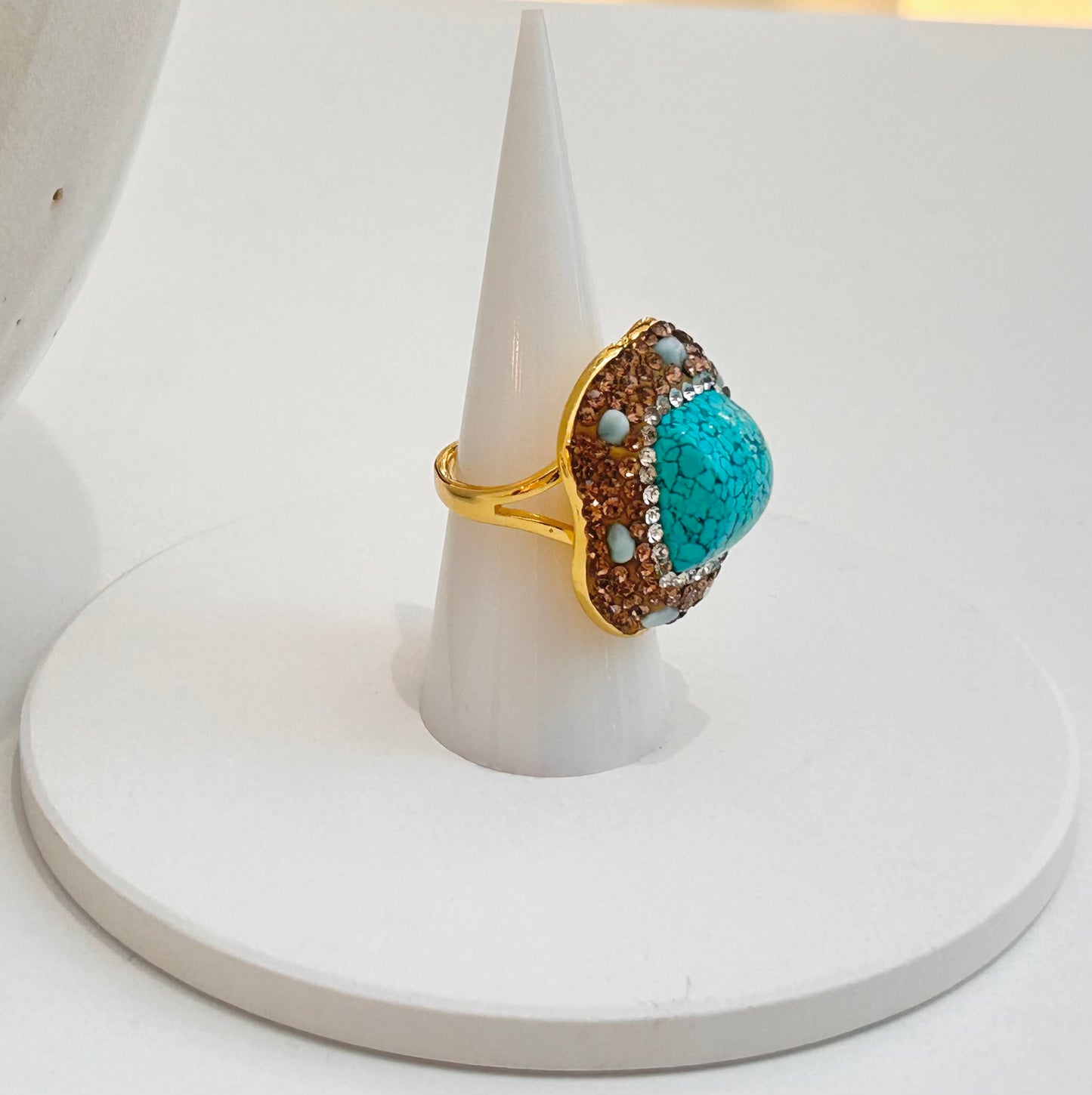 
                  
                    Azura Turquoise Statement Ring displayed on a white jewellery stand with a vibrant blue stone, dark veining and crystal detailing.
                  
                