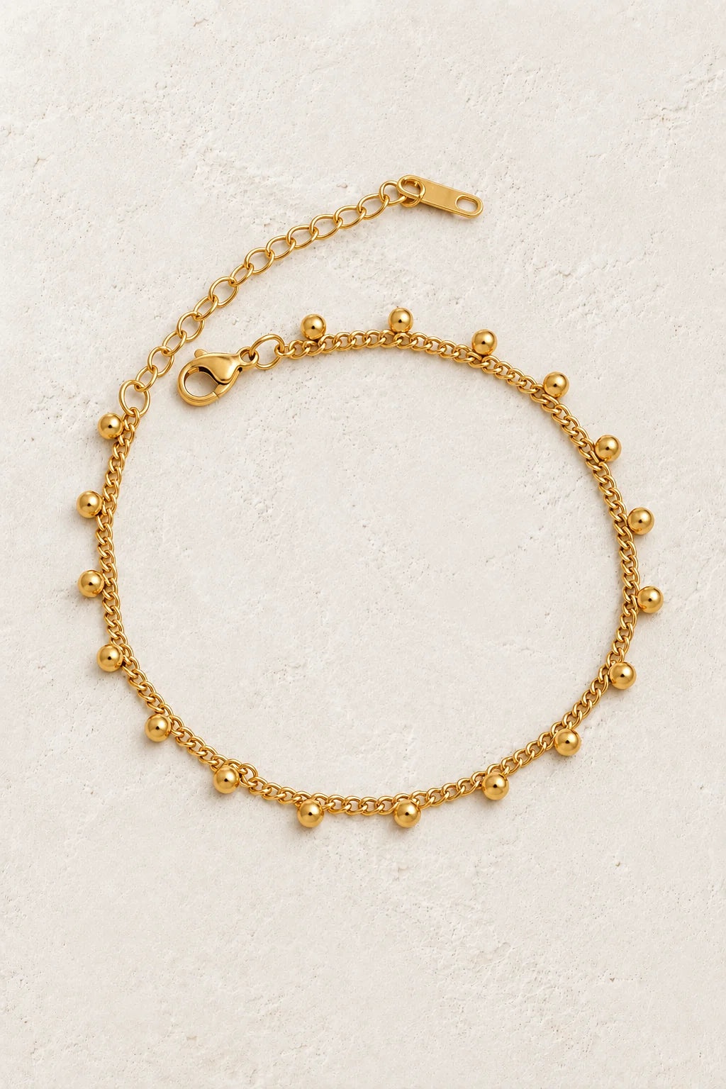 
                  
                    Dalia Gold Bead Charm Bracelet on a beige textured background
                  
                