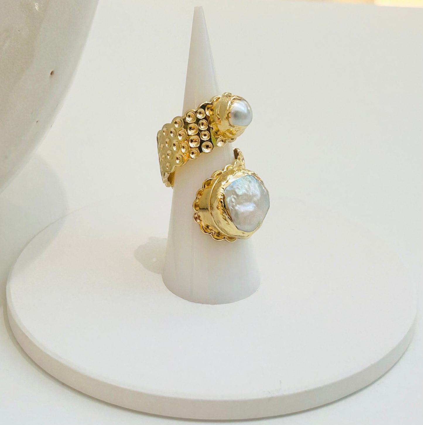 
                  
                    Calista Freshwater Pearl Statement Ring displayed on a white jewellery stand, featuring two genuine pearls and a textured open gold-plated band.
                  
                