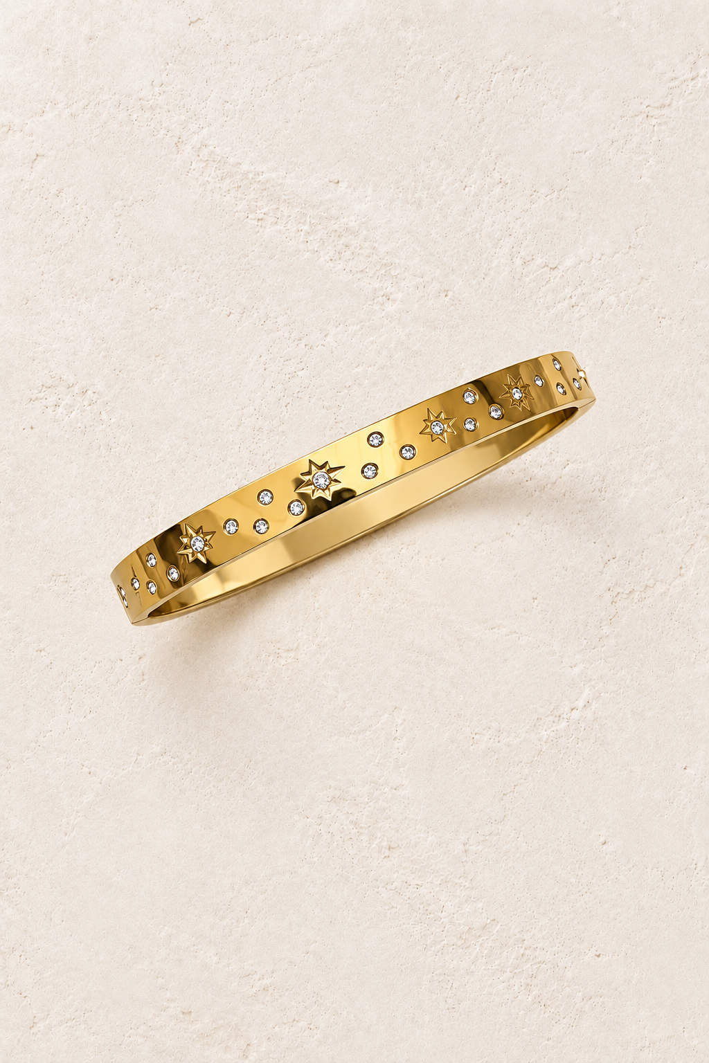 
                  
                    Celestra Gold Starburst Bangle on cream beige textured background
                  
                