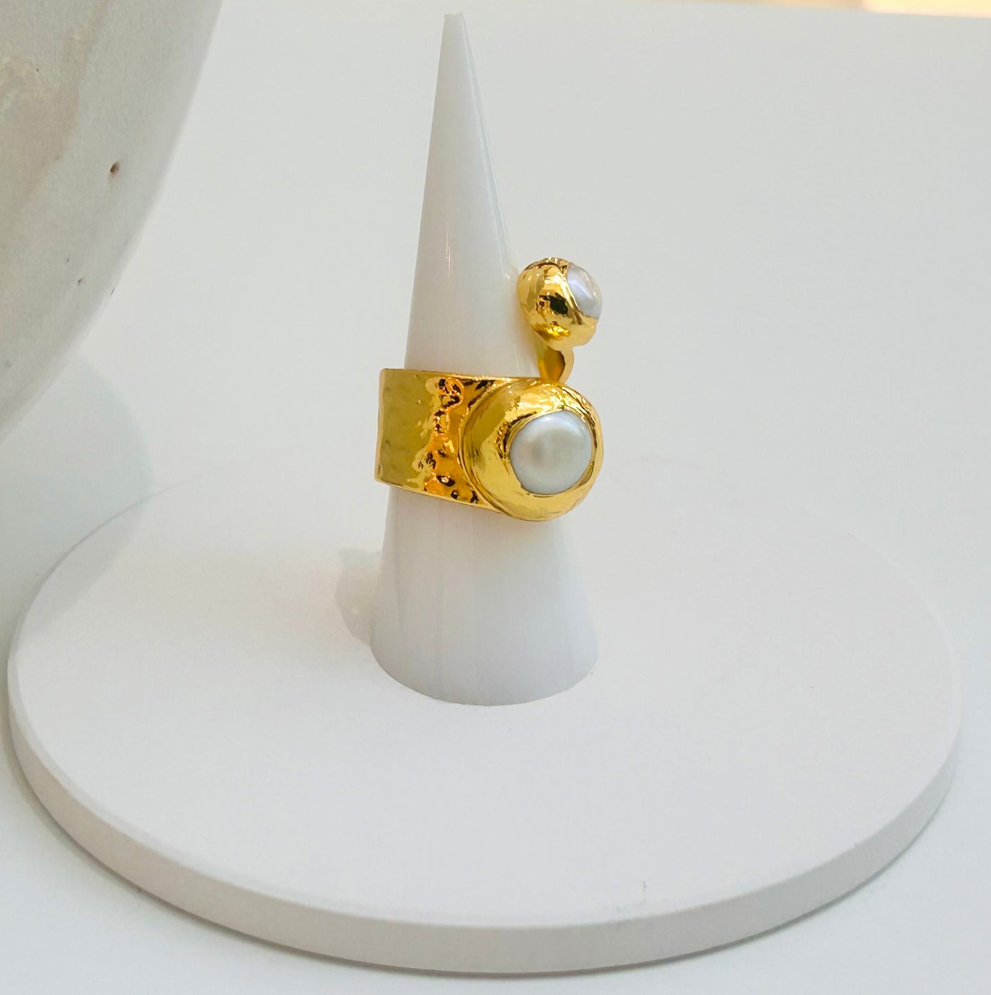 
                  
                    Elowara Freshwater Pearl Statement Ring displayed on a white jewellery stand, featuring two genuine pearls in an open sculptural gold-plated design.
                  
                