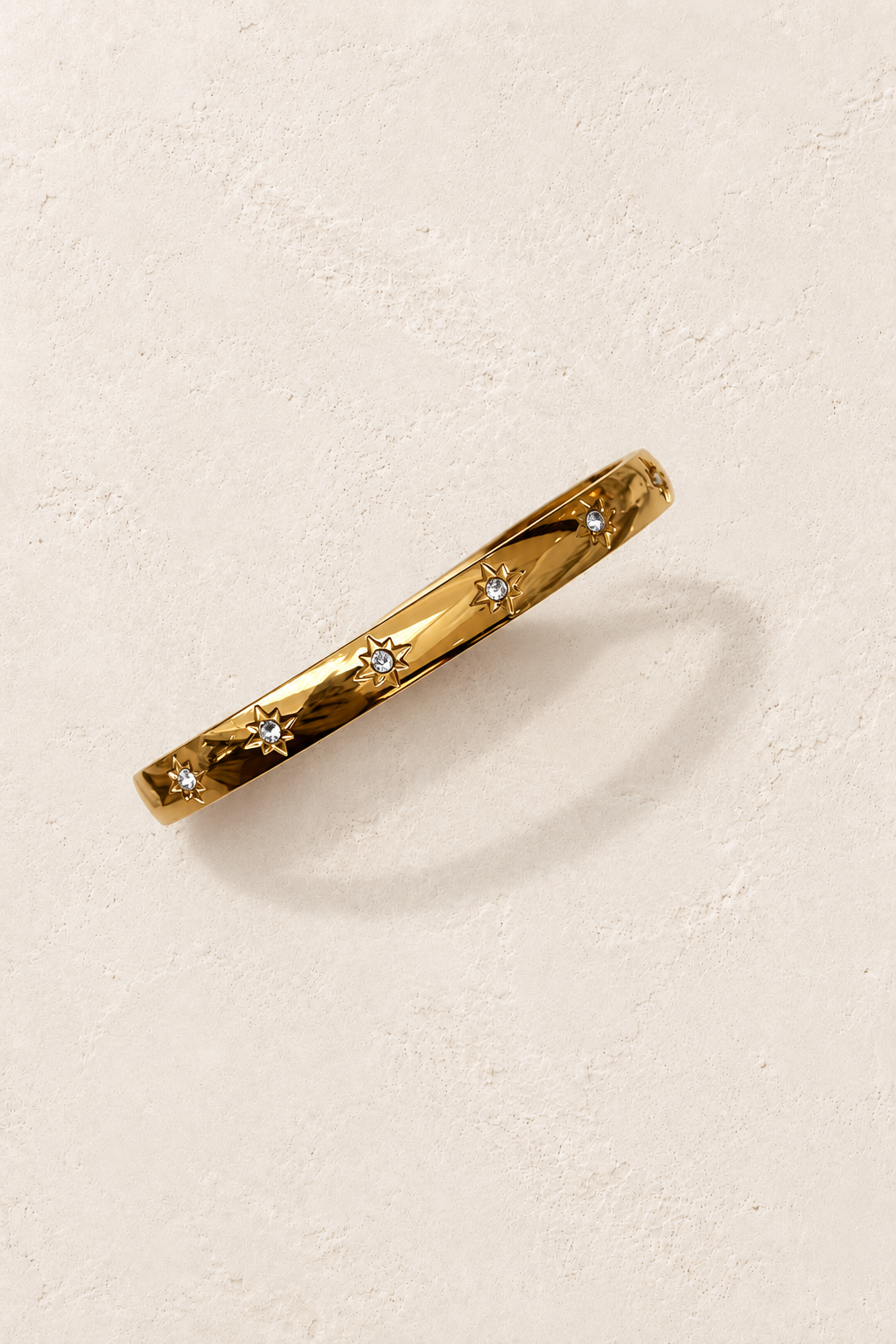 Norelle Gold Starlight Bangle on cream beige textured background