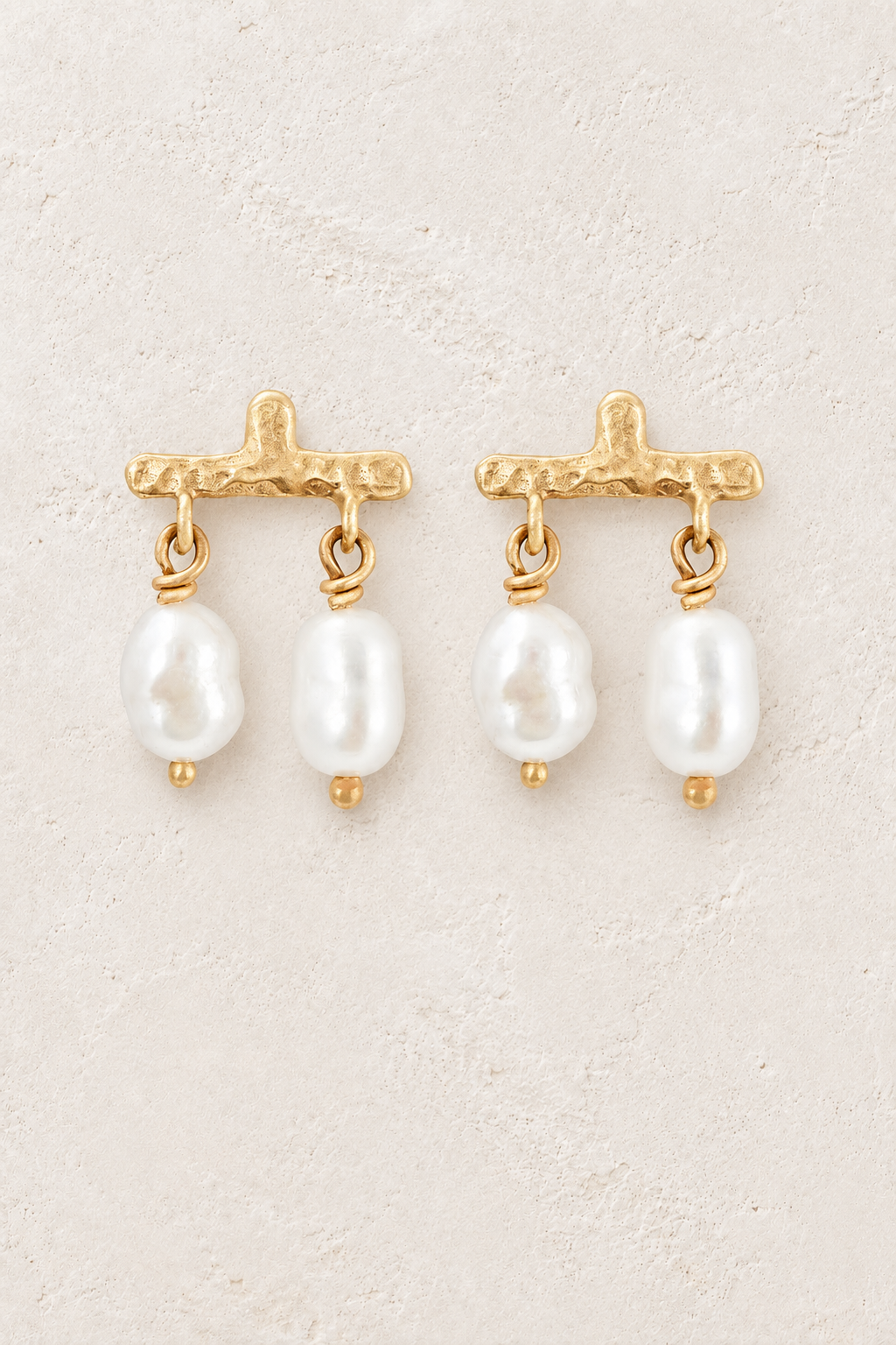 Gold textured bar stud earrings with double freshwater pearl drops on a warm off-white textured plaster background