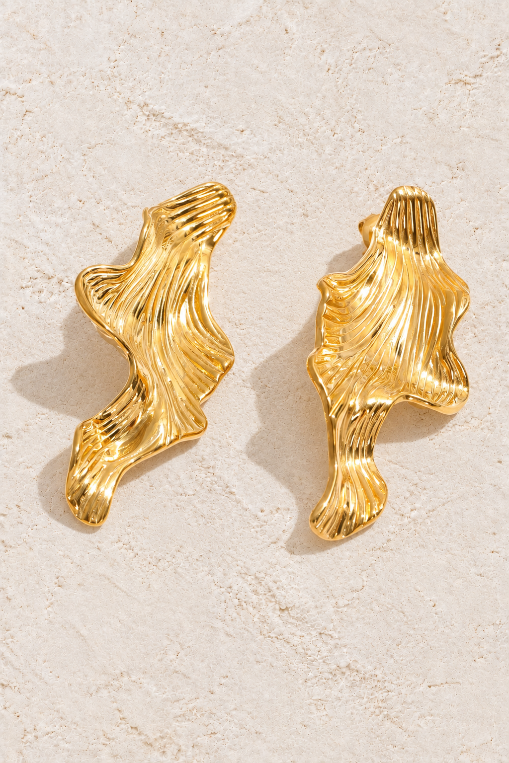 gold sculptural ridged wave earrings on cream plaster