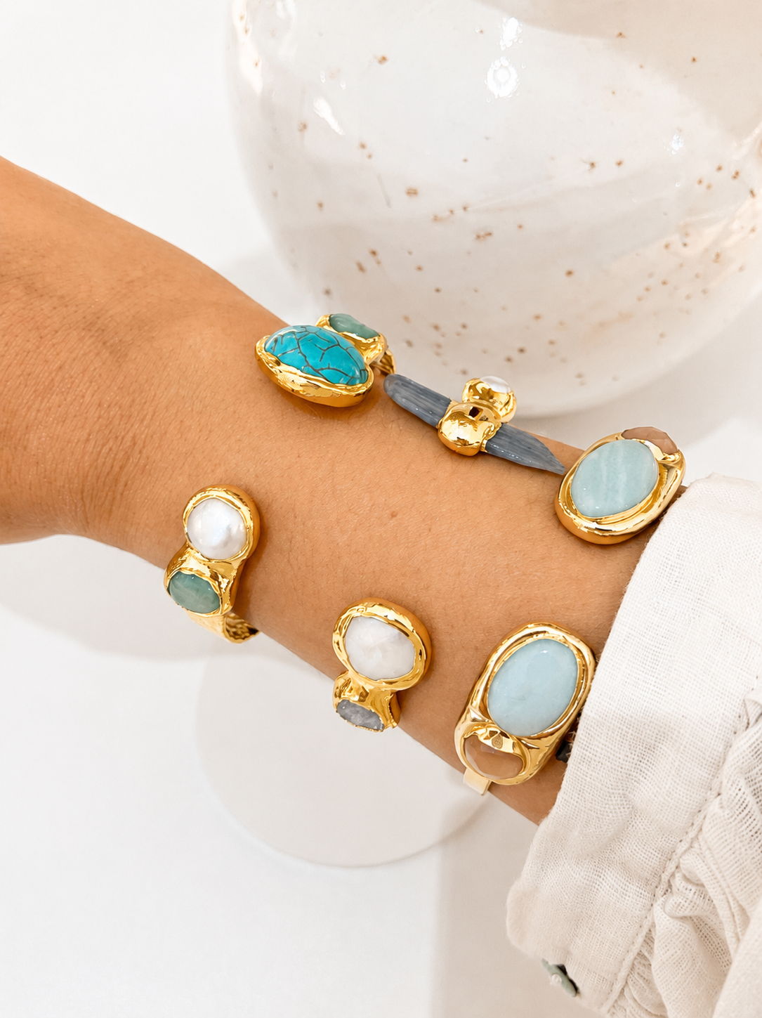 Multiple bracelets with turquoise and gold stones on a wrist against a white background