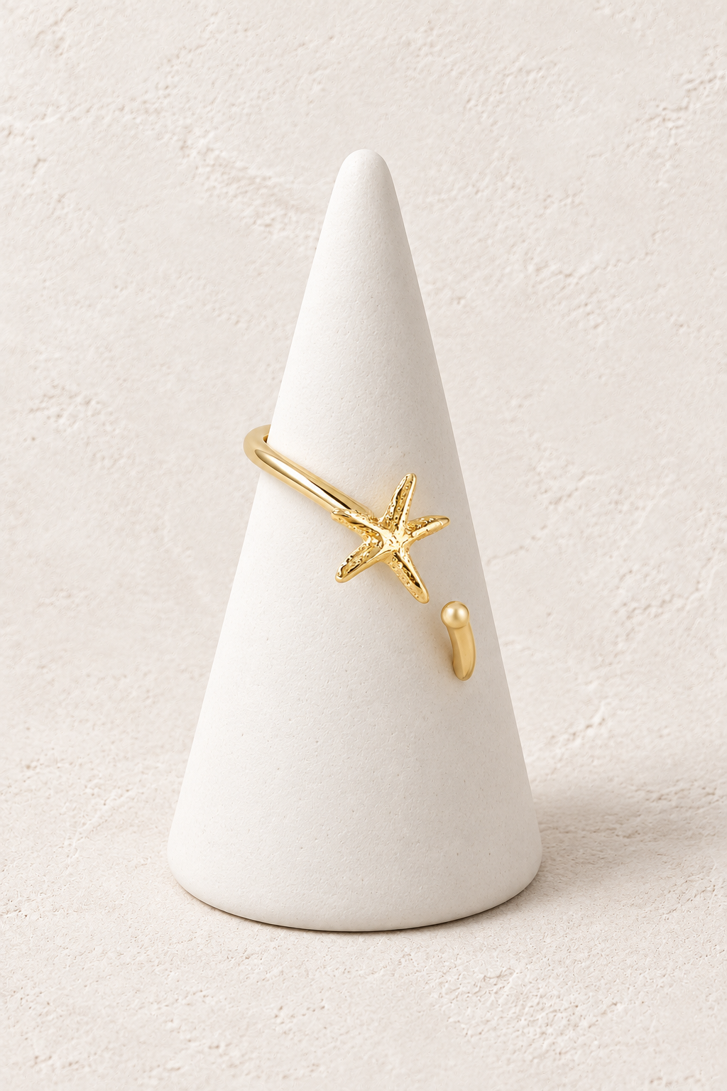 Oceana Starfish Ring on a white display cone against a warm textured background