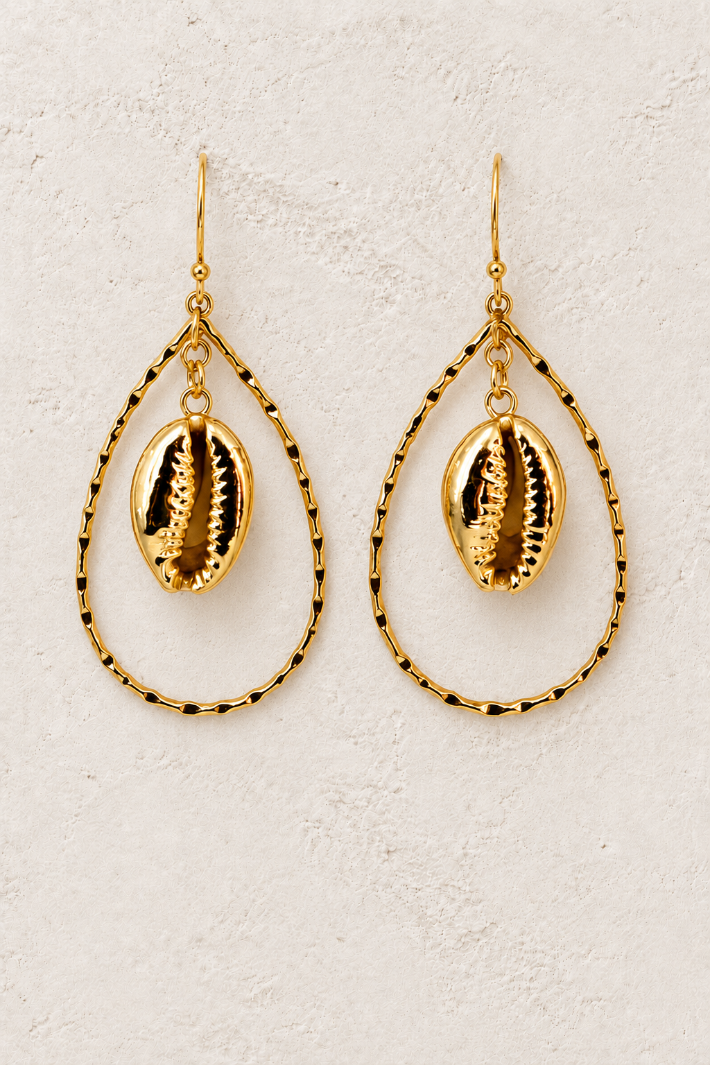 Oceanus gold cowrie shell drop earrings on a warm textured background