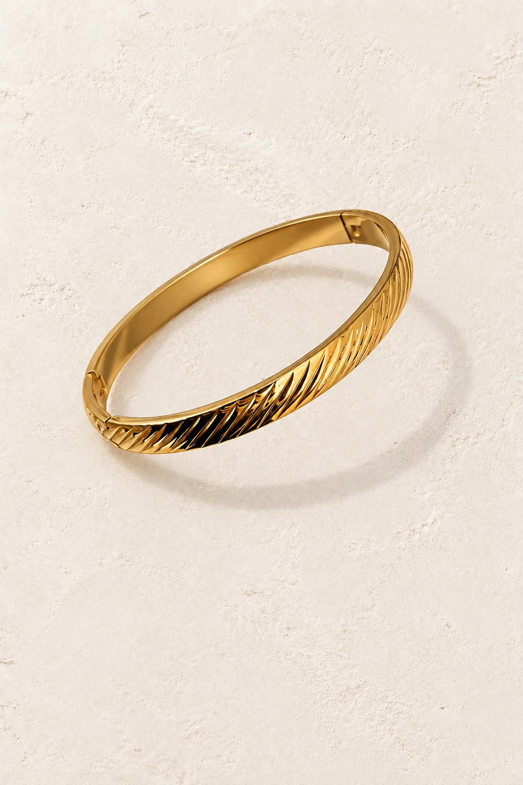 
                  
                    Oriana Gold Sculpted Twist Bangle on cream beige textured background
                  
                