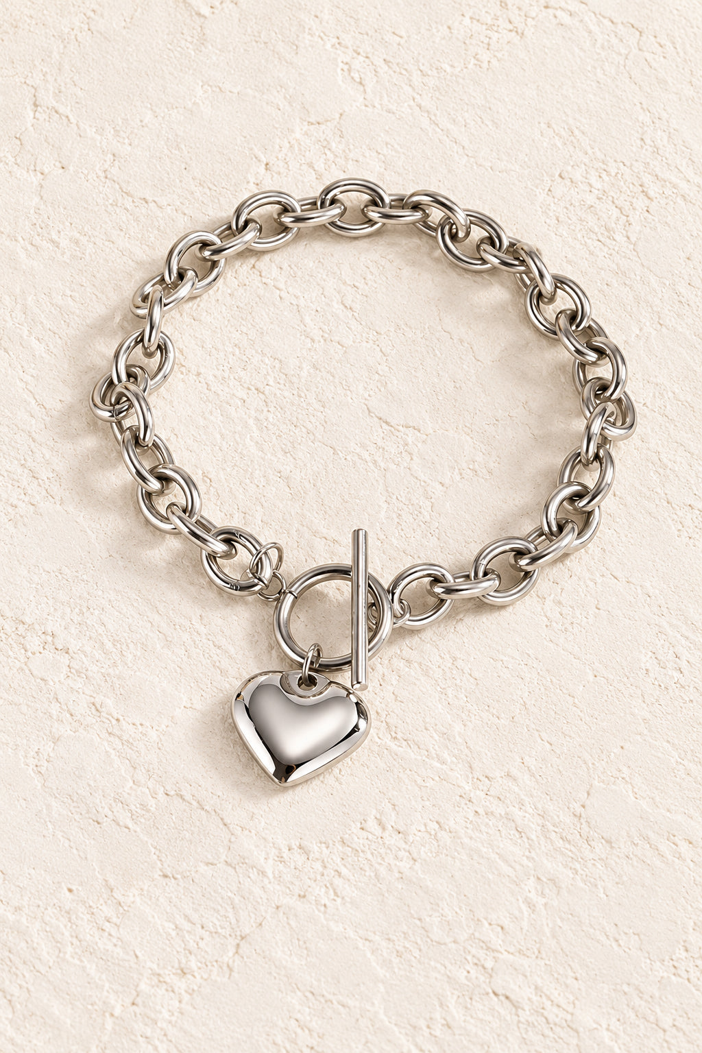 
                  
                    Silver Heart Toggle Bracelet on a beige textured background
                  
                