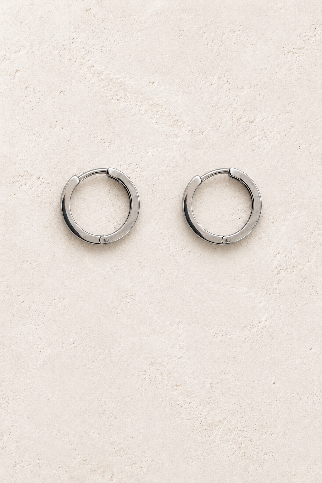 
                  
                    Riva Silver Flat Hoop Earrings on warm ivory plaster
                  
                