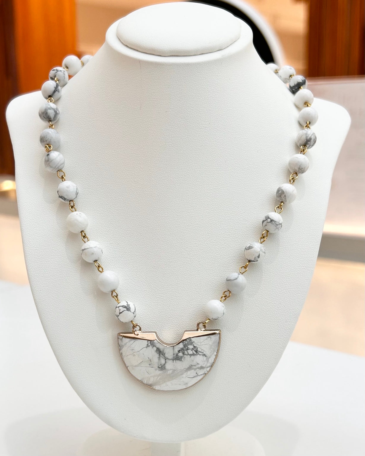 
                  
                    Savara White Howlite gold-plated statement necklace displayed on a jewellery bust
                  
                