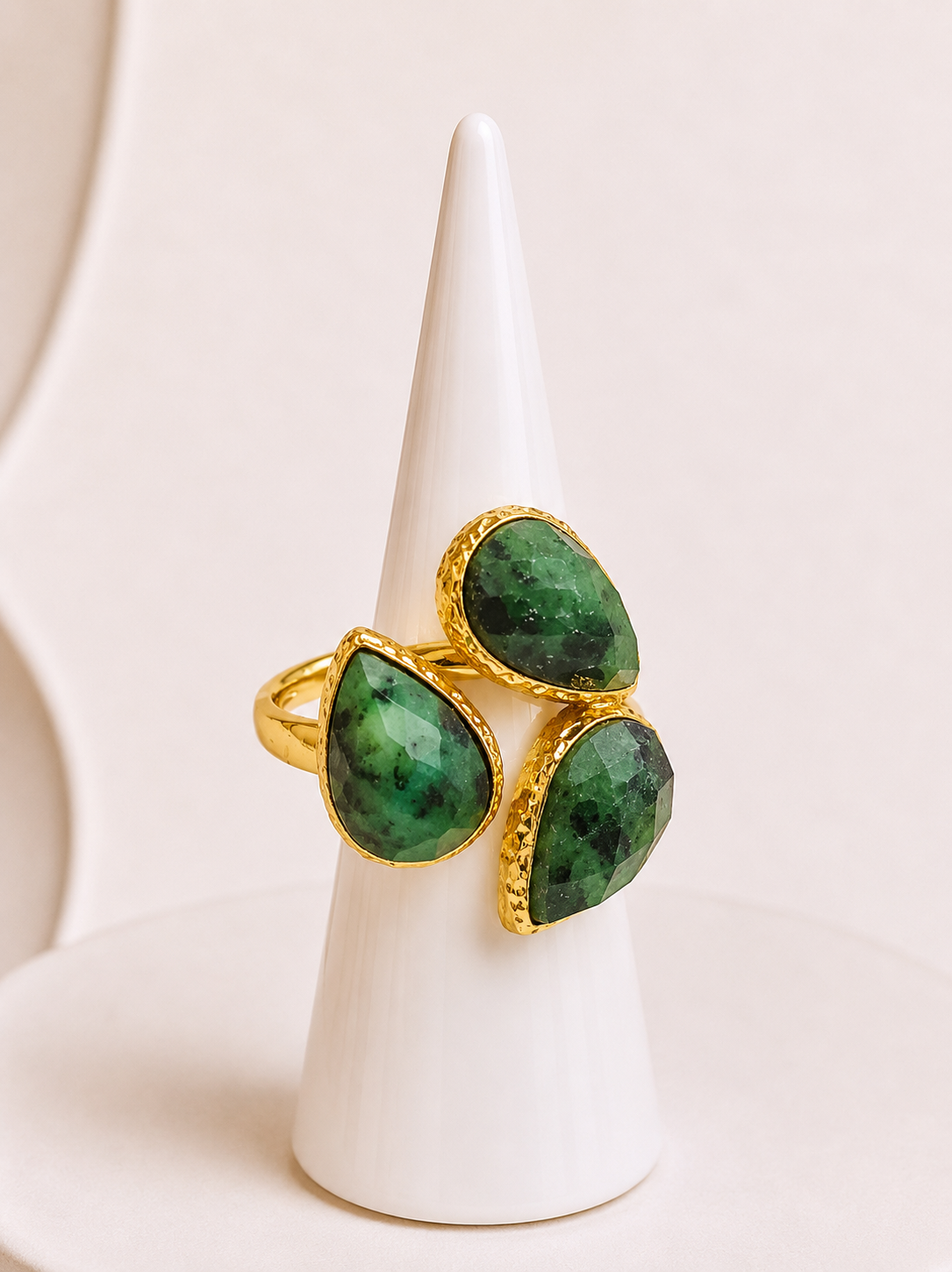 A gold ring with three green teardrop-shaped African turquoise gemstones, displayed on a white cone stand against a light beige background.