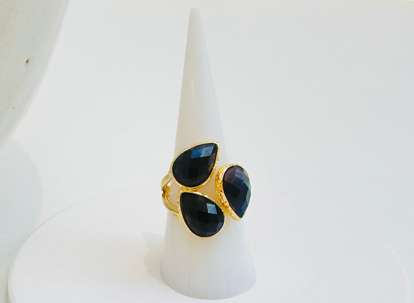 
                  
                    A gold ring with three teardrop-shaped black obsidian gemstones, displayed on a white cone stand against a white background.
                  
                