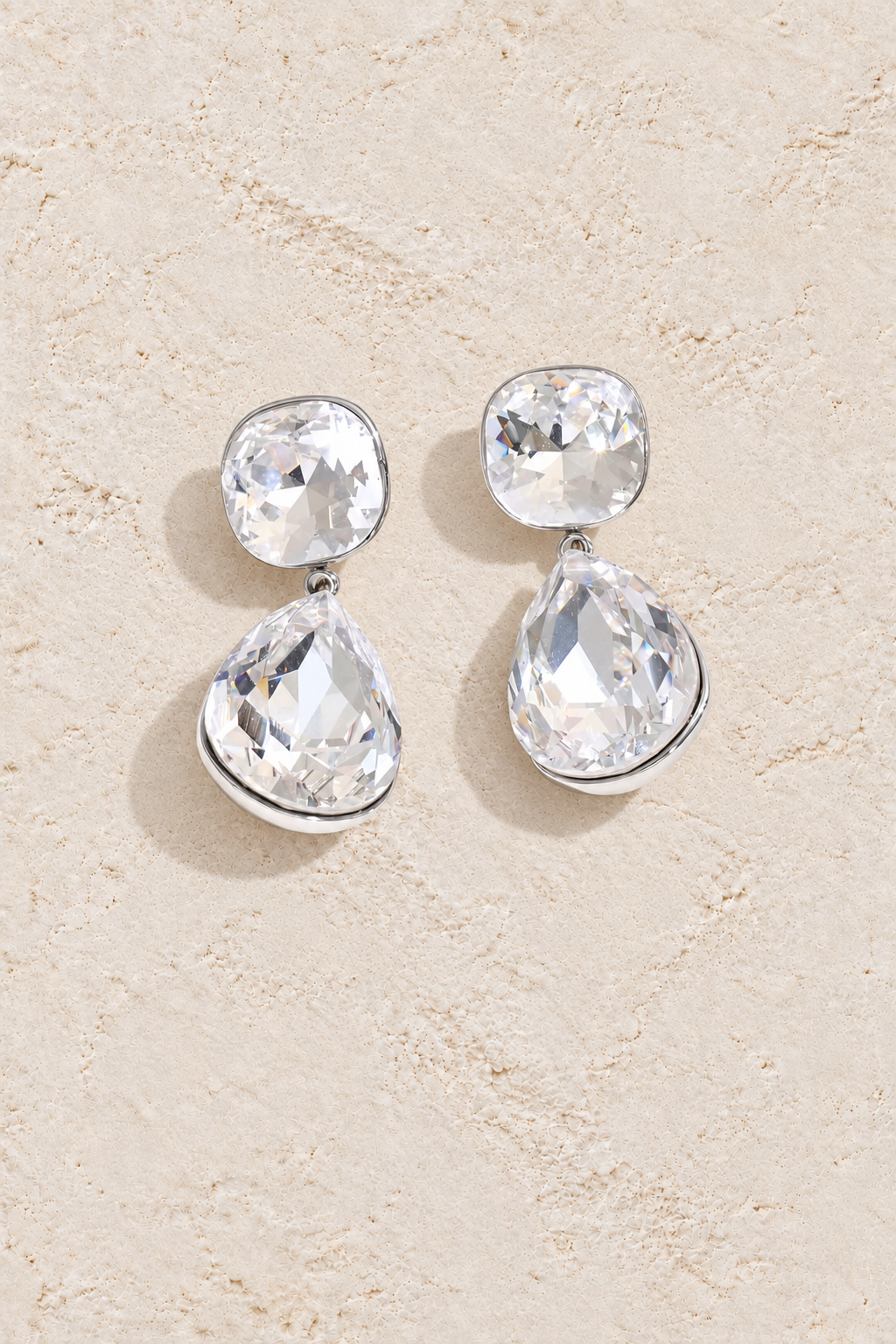 Silver cushion and pear crystal drop earrings on cream plaster