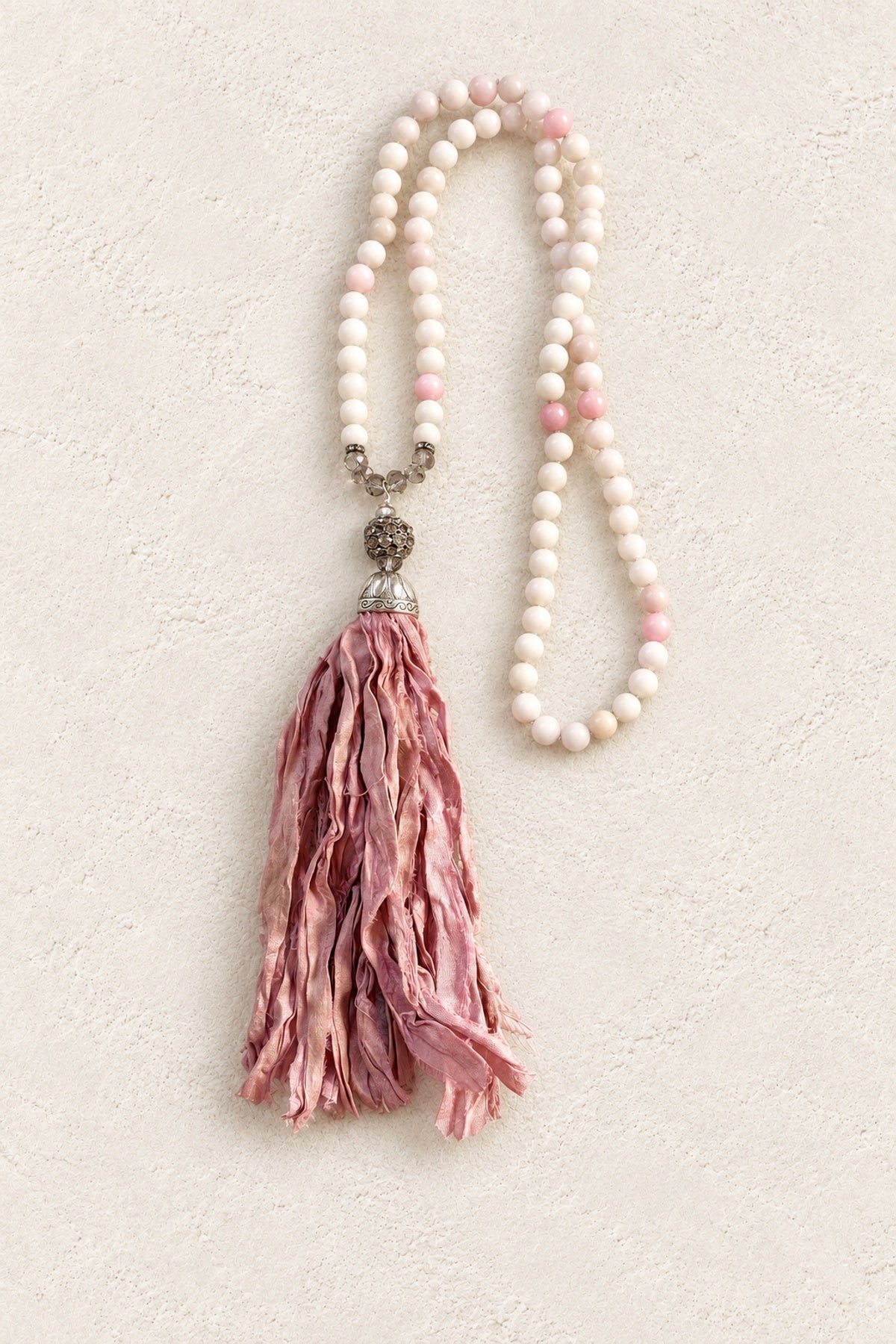
                  
                    Soft Pink Stone Silk Tassel Necklace on warm cream plaster background
                  
                
