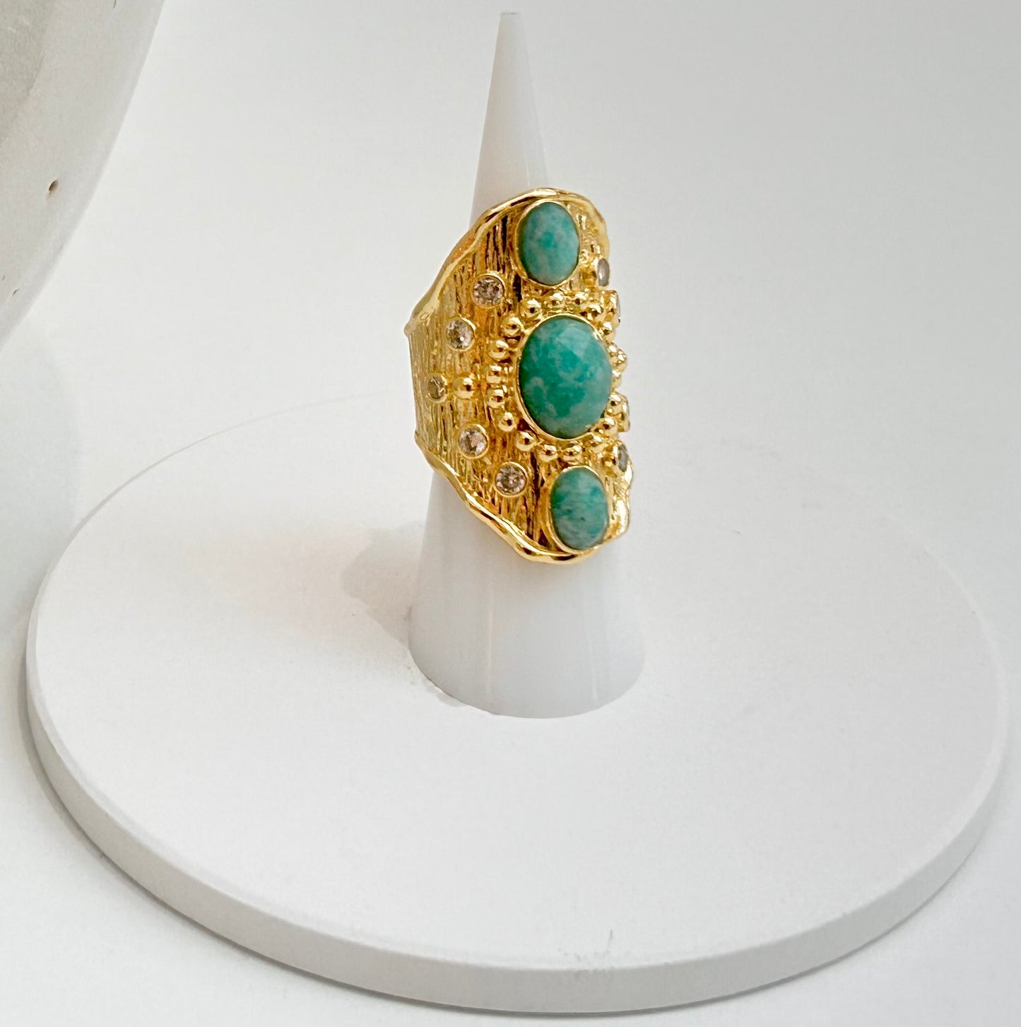 
                  
                    Solara Amazonite Statement Ring displayed on a white jewellery stand with three oval Amazonite stones and sparkling crystal detailing.
                  
                