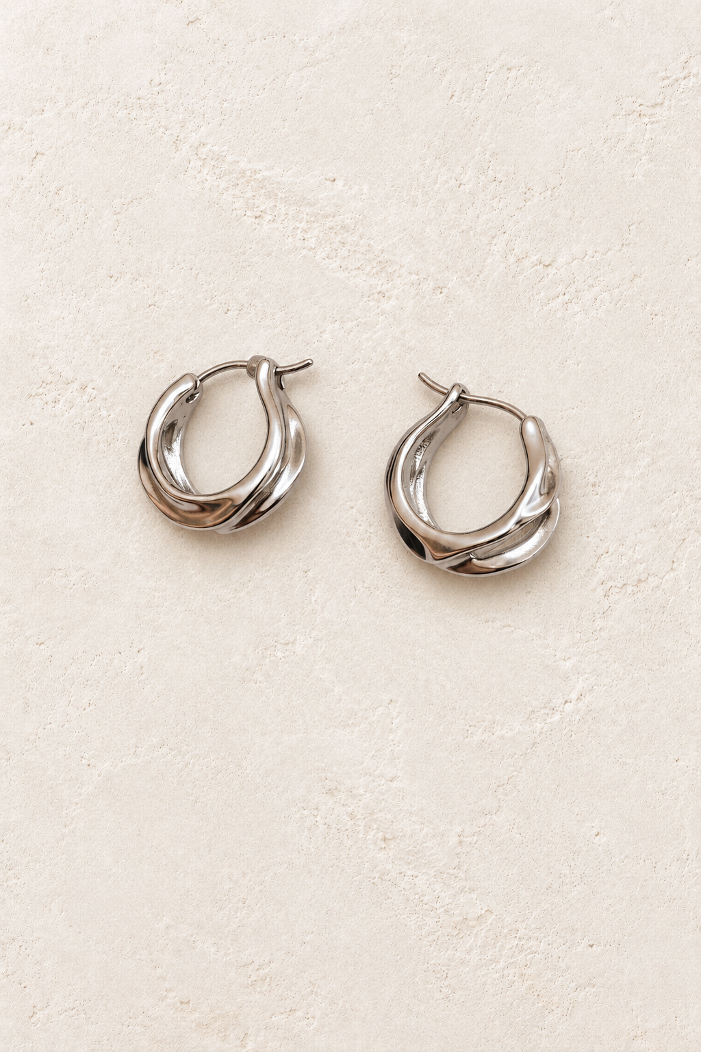
                  
                    Vionne Silver Sculpted Twist Hoop Earrings on warm ivory plaster
                  
                