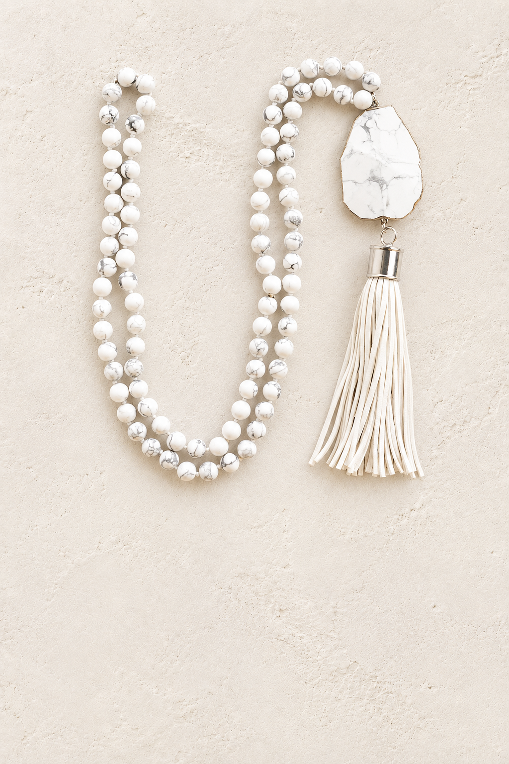 
                  
                    White Howlite Tassel Necklace on warm ivory plaster background
                  
                